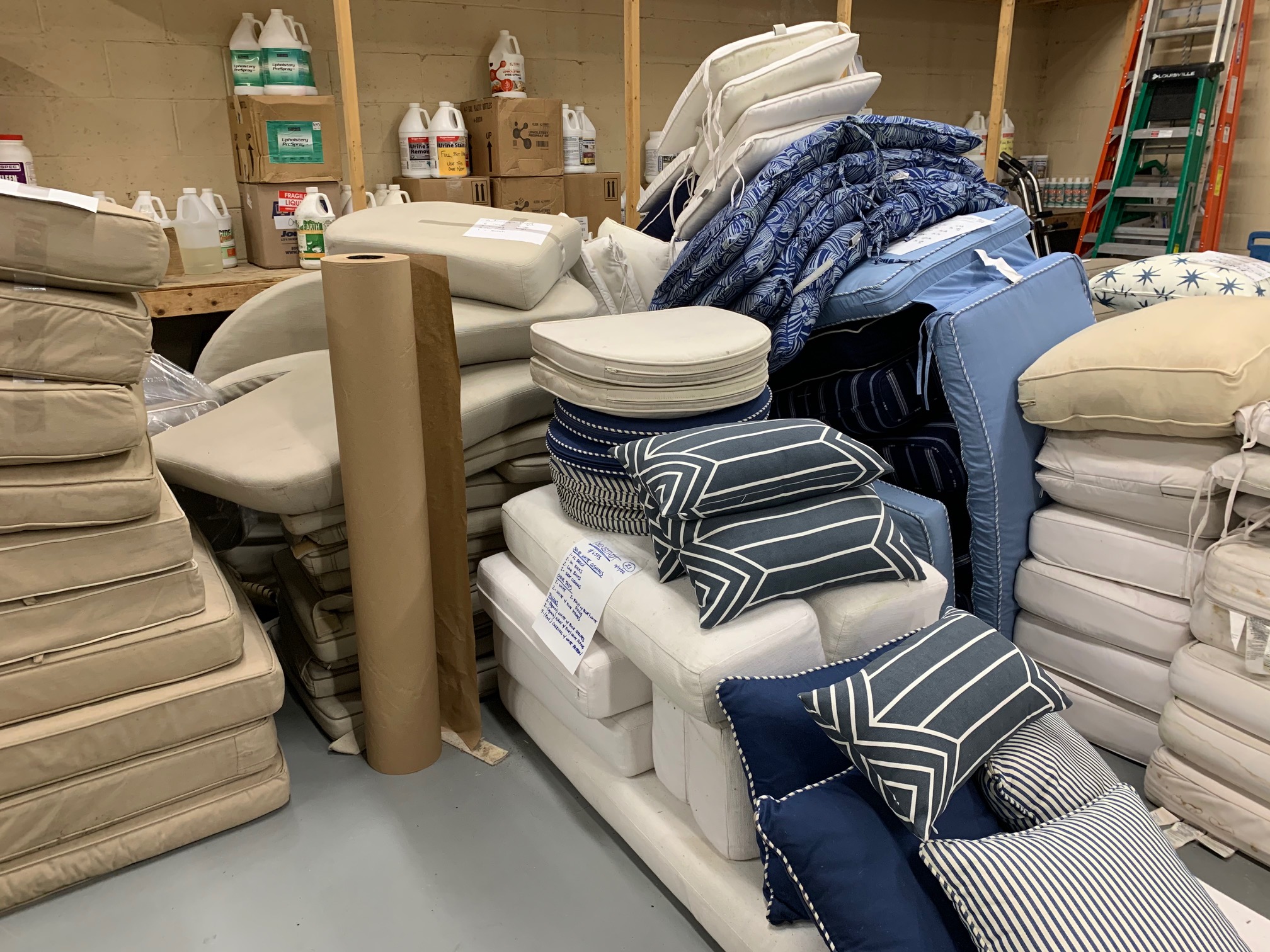 Stacks of outdoor cushions and pillows in various colors and patterns prepared for professional cleaning at Alec’s Carpet & Upholstery Cleaning in Weston, MA.