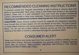 Manufacturer's upholstery cleaning instruction tag showing an S solvent cleaning code beneath a sofa cushion.